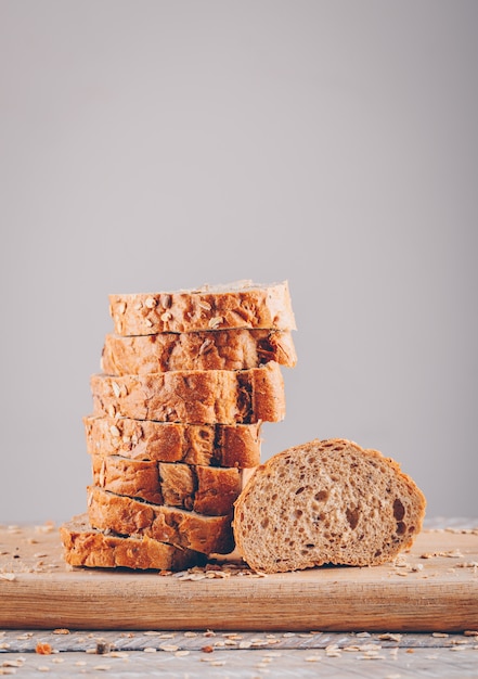 Free photo side view sliced bread in cutting board on wooden table and gray surface