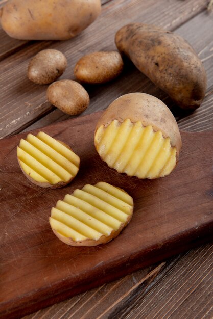 Side view of sliced and cut potato on wooden surface with whole ones on wooden background