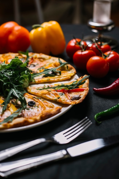 Side view of sliced italian pizza with colorful bell peppers mushrooms black olives urugula and cheese on a wooden plate