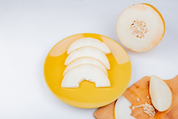 Side view of sliced melon and seeds in plate and on cutting board with cut one on white background