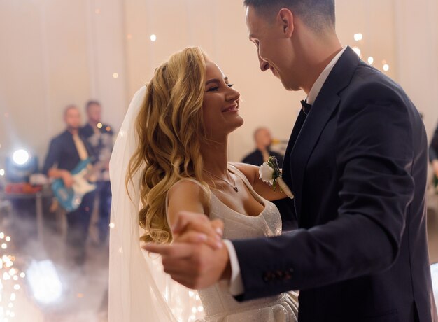 Side view of smiled young married couple, celebrating their wedding, holding hands and dancing