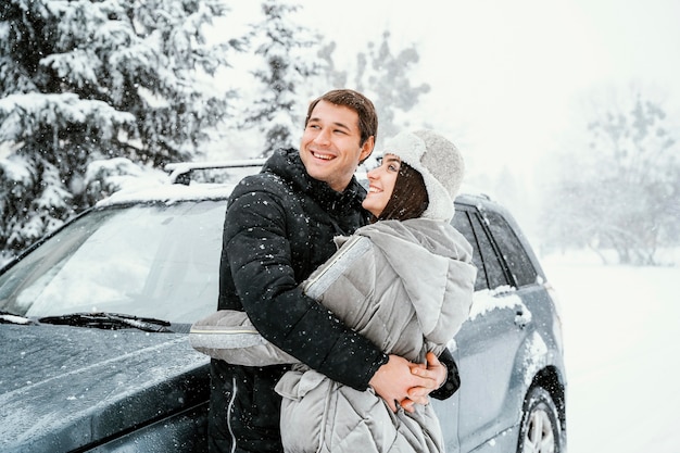 Side view of smiley couple embracing in the snow while on a road trip