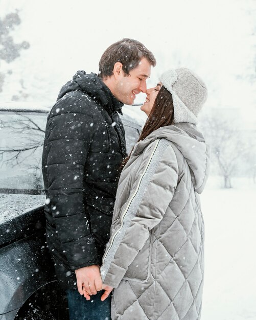 Side view of smiley couple kissing in the snow while on a road trip