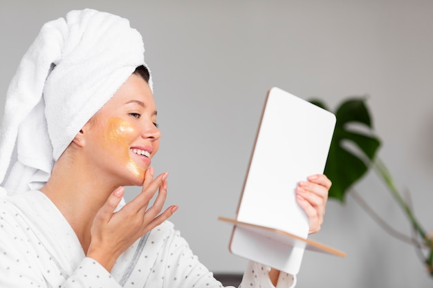 Side view of smiley woman in bathrobe applying skincare