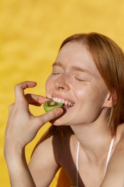 Free photo side view smiley woman eating kiwi