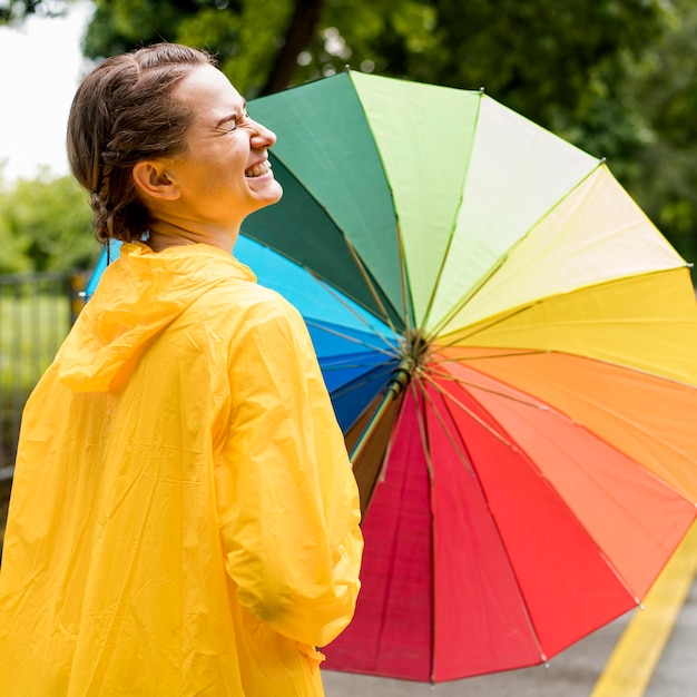 Side view smiley woman holding a colorful umbrella