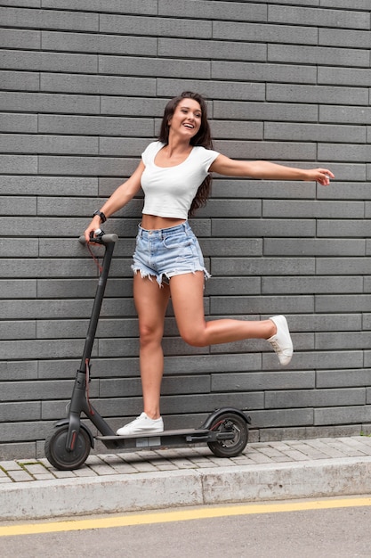 Free photo side view of smiley woman posing with scooter outside