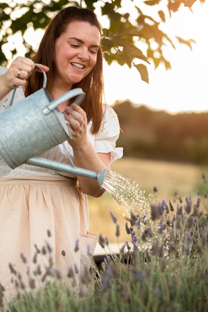 Free photo side view smiley woman watering flowers