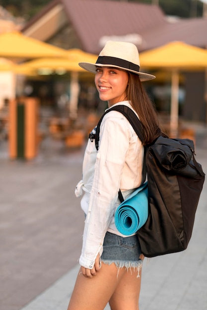 Side view of smiley woman with hat carrying backpack while traveling