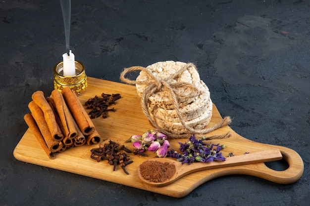 Side view of spice cloves with cinnamon sticks rice breads tied with a rope rose tea and candle on wooden board