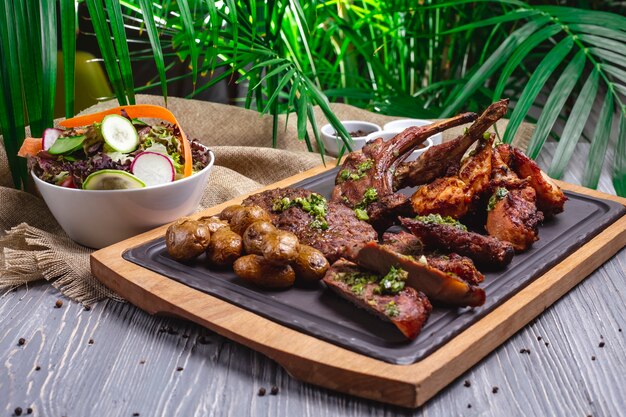 Side view steak with fried ribs with fried chicken and potatoes on the board and with vegetable salad