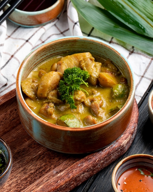 Side view of stewed chicken with vegetables in a clay bowl on plaid tablecloth