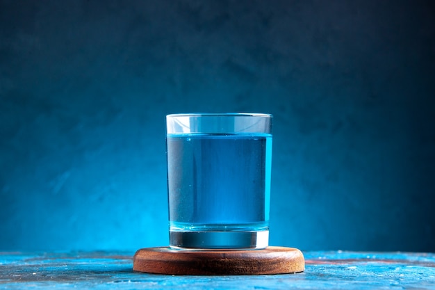 Free photo side view of a still water in a glass on wooden cutting board on blue background