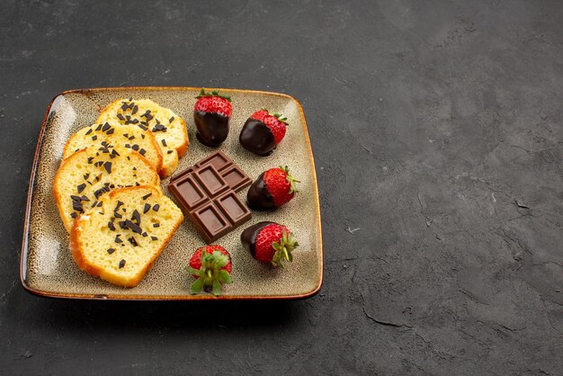 Side view strawberries and cake cake and chocolate-covered strawberries on grey plate on the left side of the table