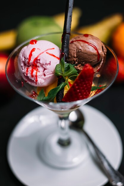 Side view of strawberry and chocolate ice cream balls in a glass vase decorated with mint