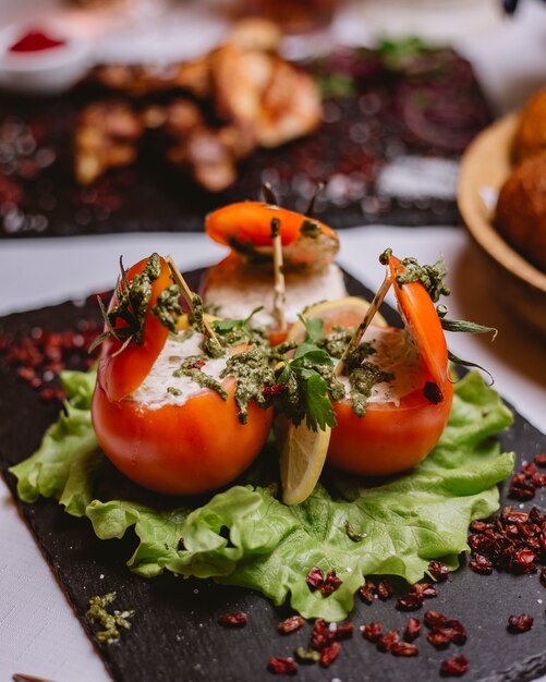 Side view stuffed tomatoes with cream sauce greens pesto sauce and dried barberry on a plate