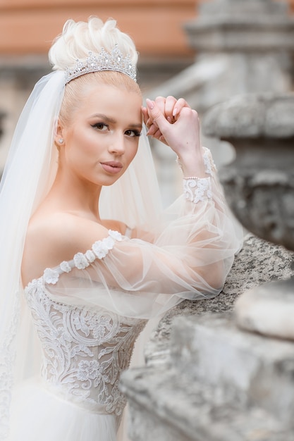 Side view of stylish bride in a chic white dress on the street looking at the camera