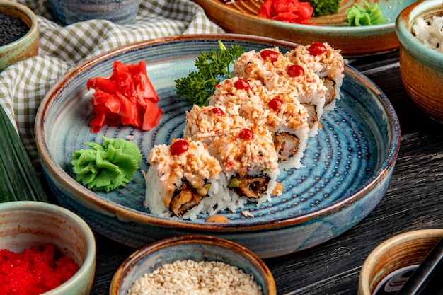 side view of sushi rolls with rice shrimp tempura avocado and cheese inside on a plate with ginger and wasabi