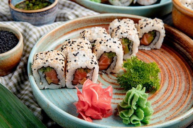 Free photo side view of sushi rolls with tuna salmon and avocado covered with sesame on a plate with wasabi and ginger