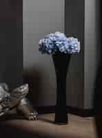 Free photo side view of tall glass black vase with blue flowers on a wooden floor