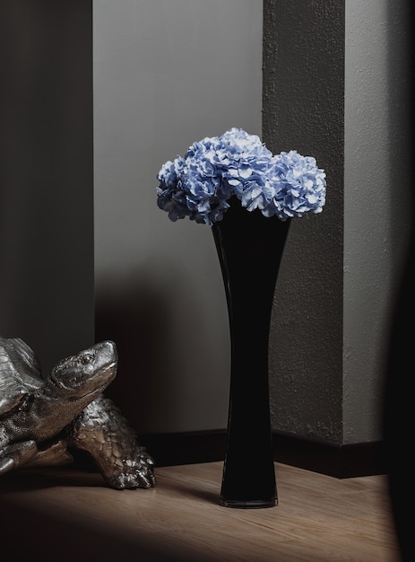 Side view of tall glass black vase with blue flowers on a wooden floor