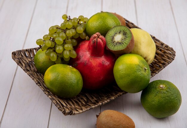 Side view tangerines with pomegranate pear apple grapes and kiwi in a basket on a white wall