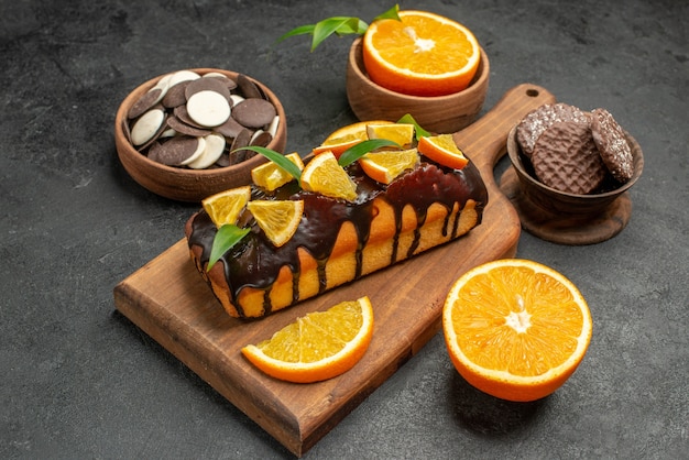 Side view of tasty cakes cut oranges with biscuits on cutting board on dark table