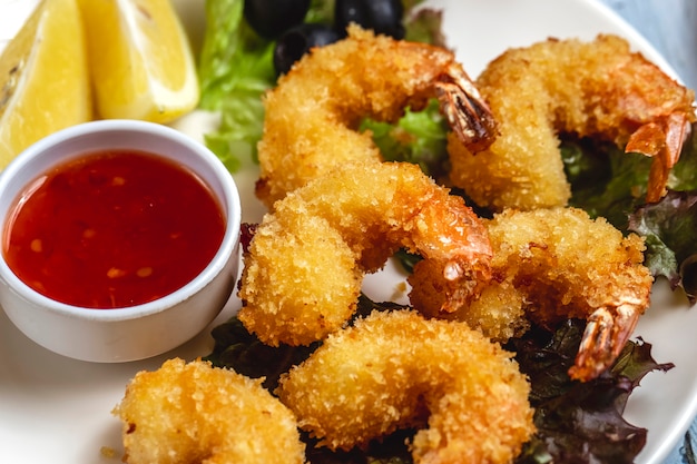 Side view tempura shrimps with sweet chili sauce slice of lemon and black olive on a plate