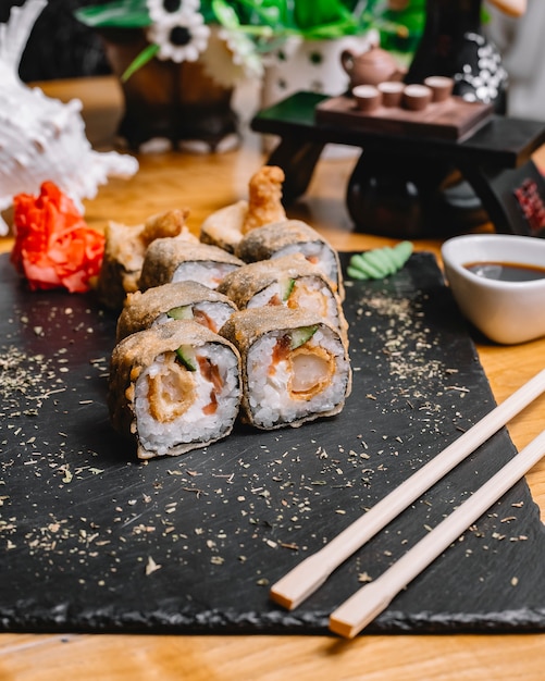 Side view tempura sushi roll with salmon cucumber ginger wasabi soy sauce and sesame seeds on a tray