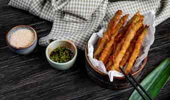 Free photo side view of tempura vegetables in a bowl served with soy sauce on wooden table with plaid fabric