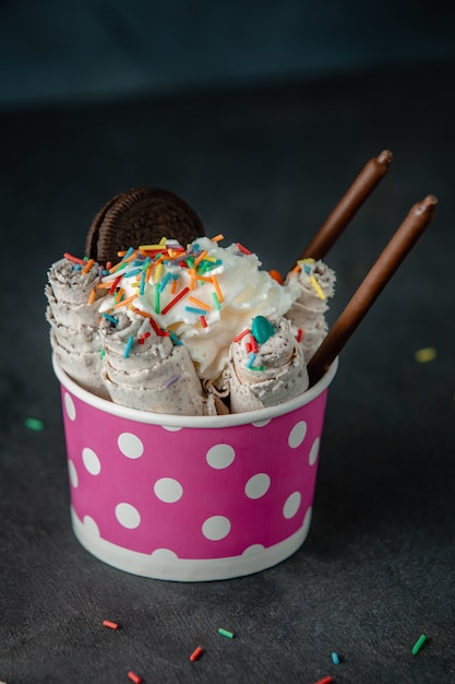 Side view of thai ice cream roll topped with colorful sprinkles in a cardboard bowl on black wall