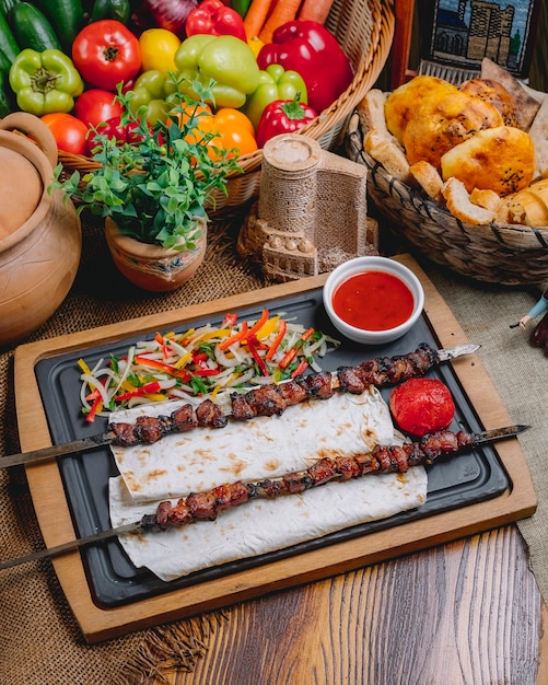 Free photo side view tike kebab on skewers on pita bread with vegetable salad and ketchup