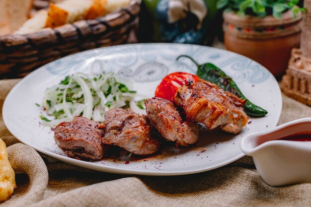 Side view tikya kebab with grilled tomato hot pepper onion and greens on a plate