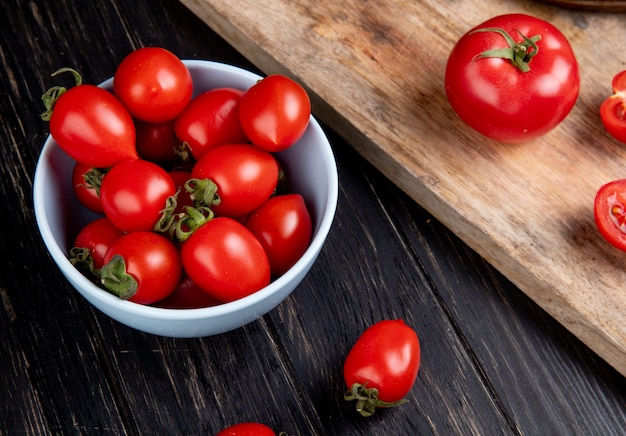 Side view of tomatoes in bowl and other ones on cutting board on wooden table