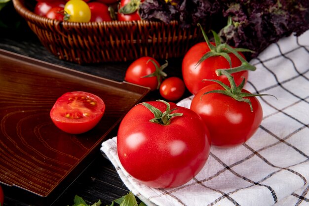 Side view of tomatoes on plaid cloth and cut tomato in tray on wooden table