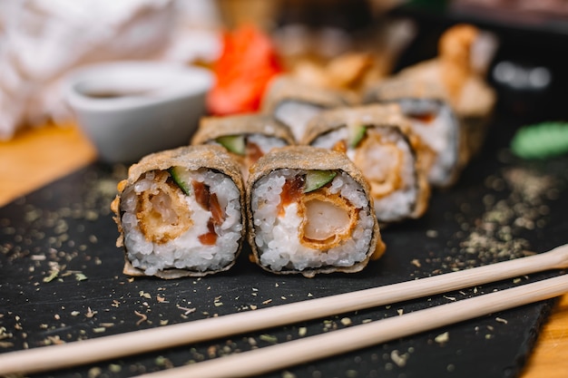 Free Photo side view of traditional japanese cuisine hot sushi roll tempura with king prawn cucumbers and cream cheese on a black board