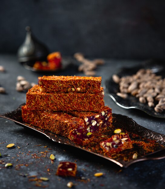 Side view of traditional turkish delight lukum with saffronpomegranate and pistachio on an antique tray on black wall