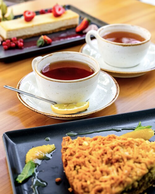 Side view two cups of tea with a slice of lemon and desserts on the table