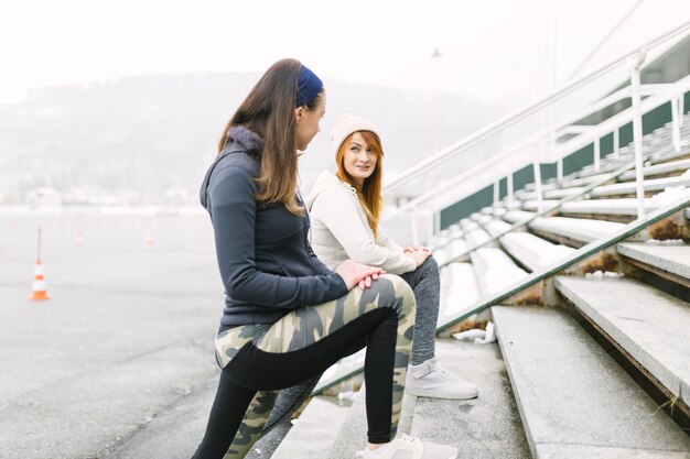 Side view of two female athlete stretching her leg on staircase in winter