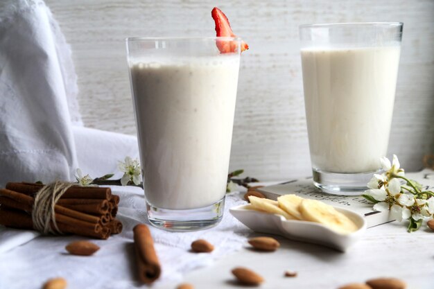 Side view two glasses of milk with cinnamonnd sliced banana and strawberrie