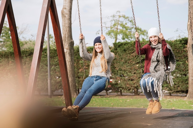 Free photo side view two smiling young women on swings