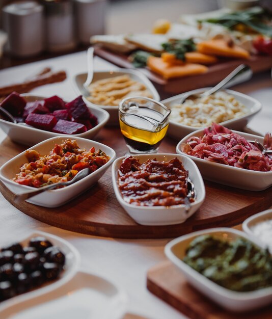 Side view of various sauces and salads with vegetables on a wooden board and olive oil in the middle