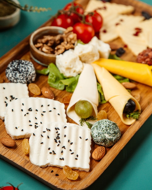 Side view of various types of cheese with nuts grapes and cherry tonatoes on wooden platter