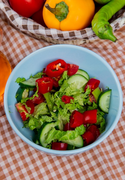 Free photo side view of vegetable salad in bowl with vegetables in basket on plaid cloth