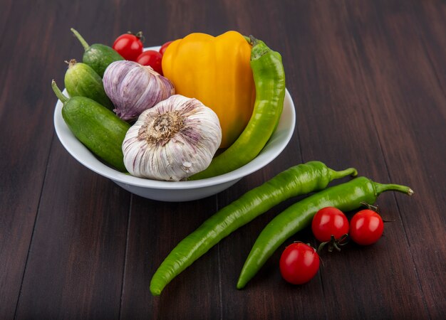 Side view of vegetables as garlic pepper cucumber and tomato in bowl on wood