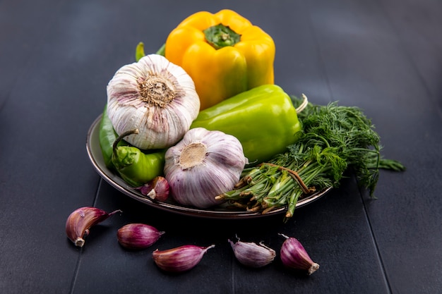 Side view of vegetables as garlic pepper dill in plate with garlic cloves on black