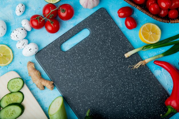 Side view of vegetables as ginger egg tomato and others with lemon and cutting board on blue surface