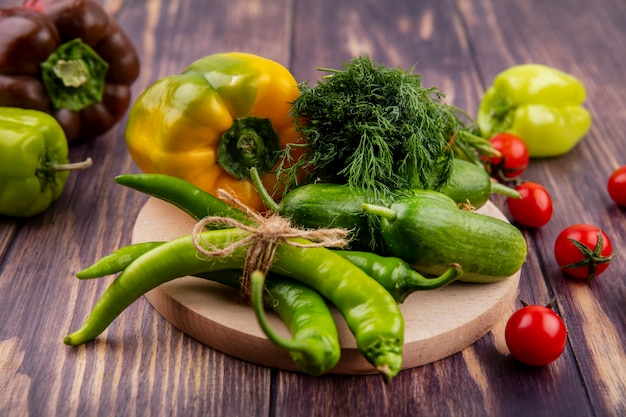 Side view of vegetables as pepper cucumber dill on cutting board with tomatoes on wood