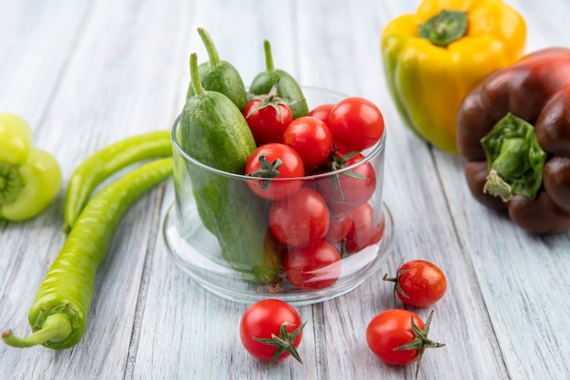 Side view of vegetables as tomato and cucumber in glass bowl with pepper on wood