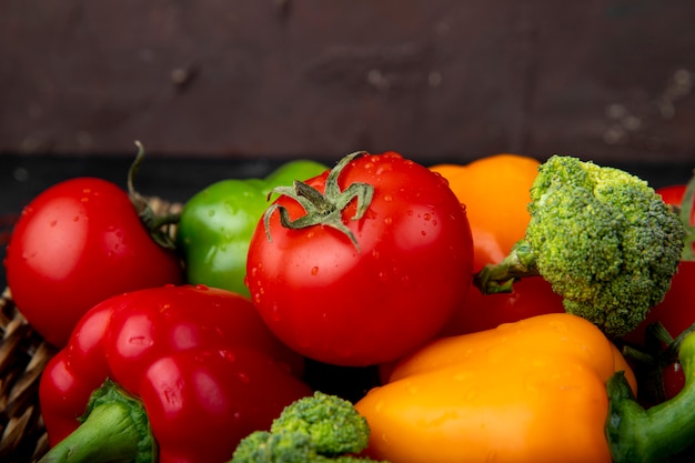 Side view of vegetables as tomatoes peppers broccoli on maroon surface